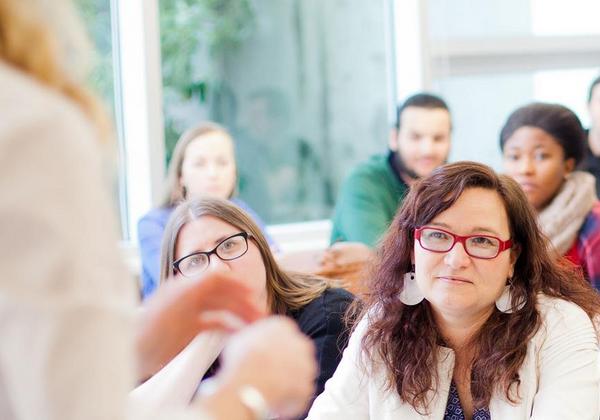 Male and female students listening to a teacher as she speaks